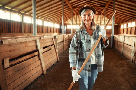 Téléchargez les photos : Mature belle agricultrice travaillant avec une fourche dans une grange sur une ferme. Concept d'agriculture et d'agriculture. - en image libre de droit