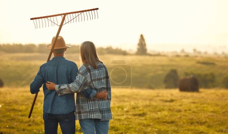 Photo for Mature beautiful couple of farmers standing with pitchforks against the background of a field on a hot day working on a farm. Farming and agriculture concept. - Royalty Free Image
