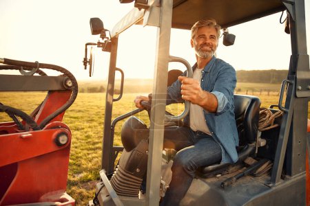 Téléchargez les photos : Un beau fermier mature assis dans un tracteur sur un champ par une chaude journée de travail dans une ferme. Concept d'agriculture et d'agriculture. - en image libre de droit