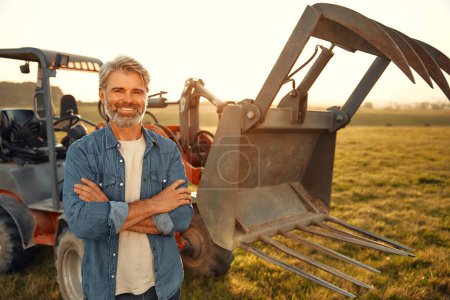 Photo for Mature handsome male farmer standing near a tractor on a field on a hot day and working on the farm. Agriculture and agriculture concept. - Royalty Free Image