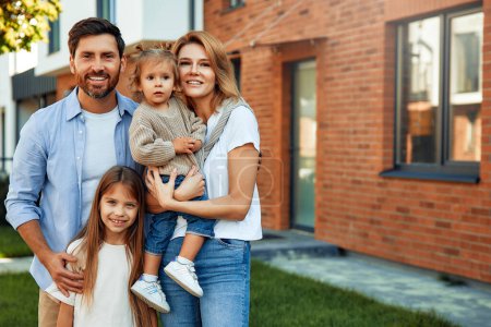 Photo for Moving of a young family to a new house. Couple with two kids daughters standing in front of their newly bought house. Renting and buying a home. - Royalty Free Image