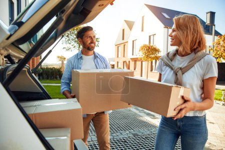 Photo for A young married couple unloads boxes of things from a car and carries them to a new home. Renting and buying a home. Moving concept. - Royalty Free Image