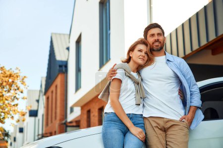 Photo for A young married couple standing near a car parked near a new house. Renting and buying a home. Moving concept. - Royalty Free Image