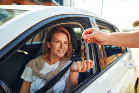 Photo for Buying a new car. A woman sitting in a car receives the keys from the seller. Transportation and ownership concept customer and salesman with car key outside. - Royalty Free Image