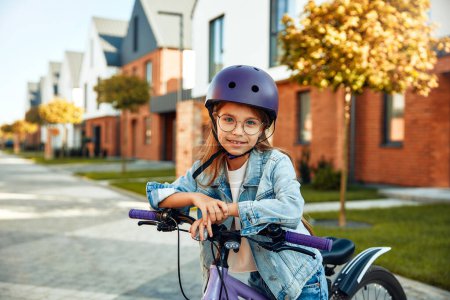 Photo for Child learning to drive a bicycle on a driveway outside. Little girl riding bikes on asphalt road in the city wearing helmets as protective gear. - Royalty Free Image
