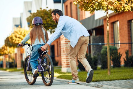 Photo for A happy father taught his little daughter to ride a bicycle. A child learns to ride a bicycle. Family activities in summer. - Royalty Free Image