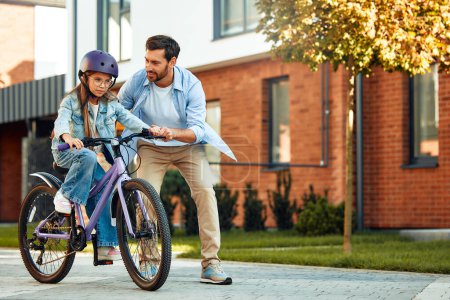 Téléchargez les photos : Un père heureux a appris à sa petite fille à faire du vélo. Un enfant apprend à faire du vélo. Activités familiales en été. - en image libre de droit
