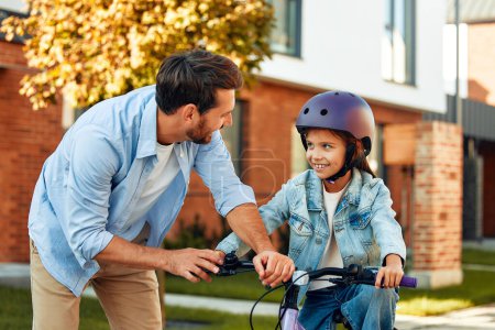 Photo for A happy father taught his little daughter to ride a bicycle. A child learns to ride a bicycle. Family activities in summer. - Royalty Free Image