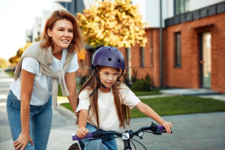 Téléchargez les photos : Une mère heureuse a appris à sa petite fille à faire du vélo. Un enfant apprend à faire du vélo. Activités familiales en été. - en image libre de droit