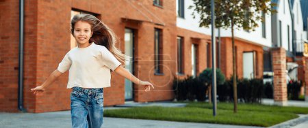 Photo for Beautiful little girl with long hair having fun and running outdoors on the background of her new home. Renting and buying real estate. Moving concept. - Royalty Free Image