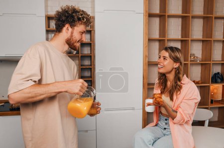 Photo for A young married couple in love having breakfast in the morning in the kitchen in a cozy home on their day off while romantically spending time together. - Royalty Free Image