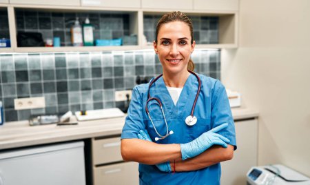 Foto de Médico veterinario femenino en uniforme azul con estetoscopio en guantes médicos de pie en la sala de examen en la clínica veterinaria. Tratamiento de mascotas. - Imagen libre de derechos