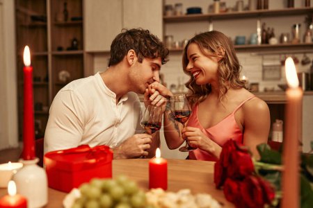 Foto de Feliz día de San Valentín. Una joven pareja enamorada de las copas de vino a la luz de las velas sentada en la cocina a la mesa, pasando románticamente la noche juntos. - Imagen libre de derechos