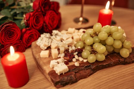 Téléchargez les photos : Joyeuse Saint-Valentin. Table de fête à gauche. Romantique dîner aux chandelles. Tranchage de fromage, bougies, bouquet de roses, cadeau et verres de vin sur la table. - en image libre de droit