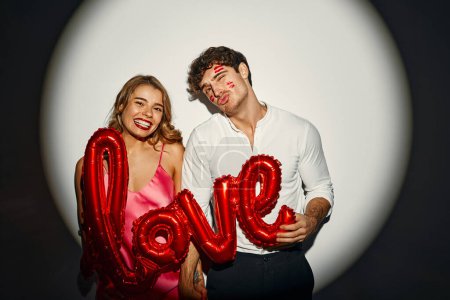 Téléchargez les photos : Joyeuse Saint-Valentin. Couple amoureux tenant un ballon avec l'inscription amour sur un fond blanc sous la lumière d'un projecteur. - en image libre de droit