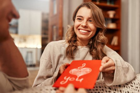 Téléchargez les photos : Joyeuse Saint-Valentin. Une femme donne une carte de vœux à son bien-aimé avec l'inscription Je t'aime dans le salon à la maison. - en image libre de droit