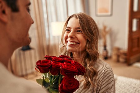 Téléchargez les photos : Joyeuse Saint-Valentin. Un homme donne un bouquet de roses rouges à sa bien-aimée femme dans le salon de la maison. Soirée romantique ensemble. - en image libre de droit