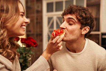 Téléchargez les photos : Joyeuse Saint-Valentin. Jeune couple amoureux manger des gâteaux assis sur la table dans la cuisine, passer la soirée ensemble romantiquement. - en image libre de droit