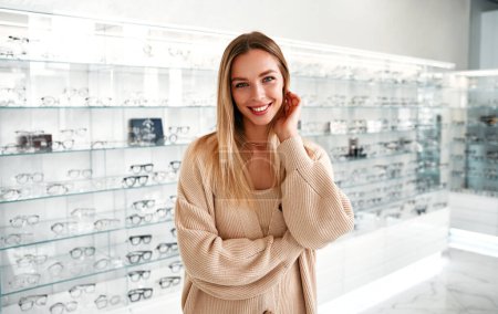 Photo for Portrait of a woman standing against the background of shelves with glasses in an professional store with various eyeglasses. Health care, eyeball check, clear vision concept. - Royalty Free Image
