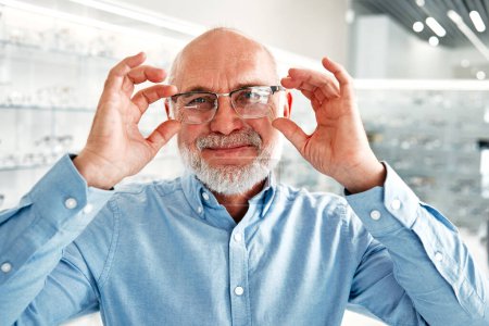 Foto de Hombre maduro senior eligiendo gafas ópticas para sí mismo en una tienda profesional. Corrección de la visión y oftalmología. - Imagen libre de derechos