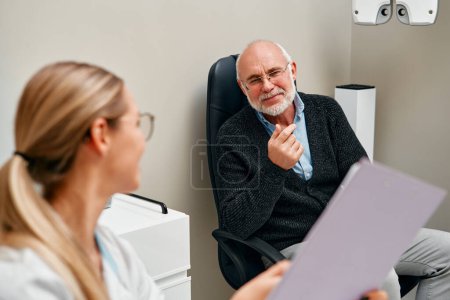 Photo for A female ophthalmologist discusses a diagnosis with a mature patient while sitting at a computer in an ophthalmology clinic. Vision correction and selection of glasses and lenses. - Royalty Free Image