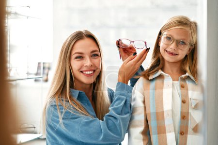 Photo for Mom with her child daughter choosing optical glasses in a professional store. Vision correction and ophthalmology. - Royalty Free Image