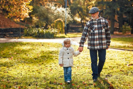 Photo for Grandfather walking and playing with his cute little granddaughter in the park in autumn. - Royalty Free Image