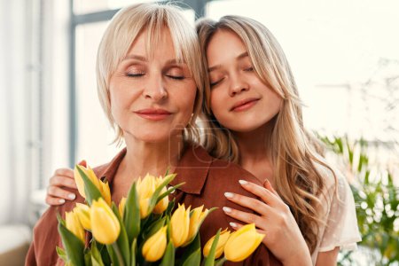 Téléchargez les photos : Joyeuse fête des mères et fête des femmes. Charmante mère et fille avec un bouquet de tulipes dans le salon près de la fenêtre. L'amour et les soins de mère. - en image libre de droit