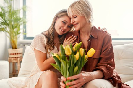 Photo for Happy Mother's Day and Women's Day. Charming mother and daughter with a bouquet of tulips in the living room near the window. Mother's love and care. - Royalty Free Image
