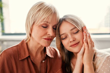 Photo for Happy Mother's Day and Women's Day. Charming daughter and mother tenderly hugging while sitting in the living room by the window. Mother's love and care. - Royalty Free Image