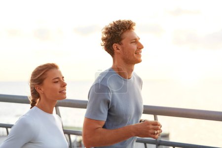 Photo for A couple in sportswear jogging outdoors on a bridge. Morning exercises and jogging. Sports and recreation, active lifestyle. - Royalty Free Image