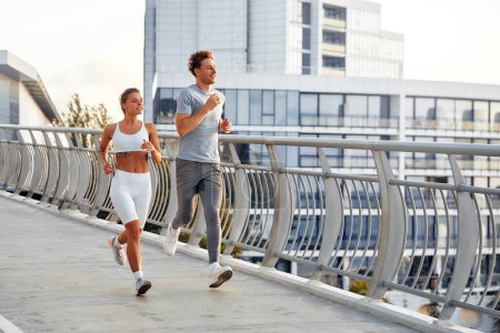 Téléchargez les photos : Un couple en tenue de sport faisant du jogging à l'extérieur sur un pont. Exercices matinaux et jogging. Sports et loisirs, mode de vie actif. - en image libre de droit
