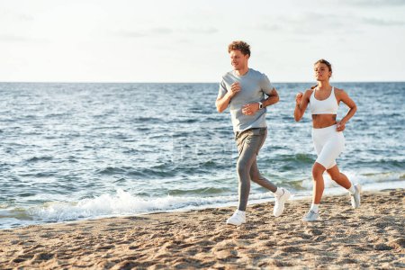 Photo for A couple in sportswear running along the shore by the sea. Morning exercises and jogging. Sports and recreation, active lifestyle. - Royalty Free Image