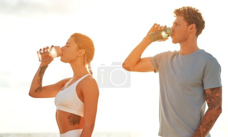 Téléchargez les photos : Un couple en tenue de sport se reposant après avoir couru sur le rivage près de la mer et de l'eau potable. Exercices matinaux et jogging. Sports et loisirs, mode de vie actif. - en image libre de droit