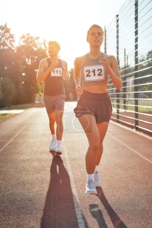 Photo for Couple in sportswear with numbers running at the stadium. Morning exercises and jogging. Sports and Olympic Games, active lifestyle. - Royalty Free Image