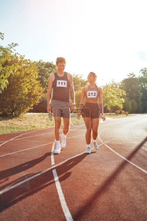 Photo for A couple of runners in sportswear with numbers resting after a run at the stadium. Morning exercises and jogging. Sports and Olympic Games, active lifestyle. - Royalty Free Image