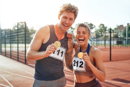 Téléchargez les photos : Une paire de coureurs vainqueurs en vêtements de sport avec des numéros montrant des médailles d'or pour la première place. Sports et Jeux Olympiques, concept de victoire. - en image libre de droit