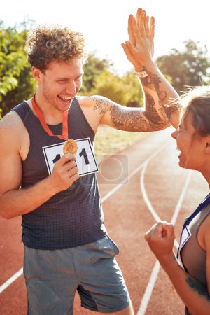 Photo for A pair of winner runners in sportswear with numbers showing gold medals for first place and high-fiving each other. Sports and Olympic Games, victory concept. - Royalty Free Image