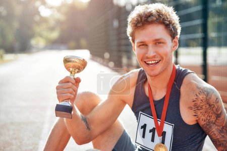 Photo for Male winner in sportswear with number with gold medal for first place and cup celebrating after competition. Sports and Olympic Games, victory concept. - Royalty Free Image