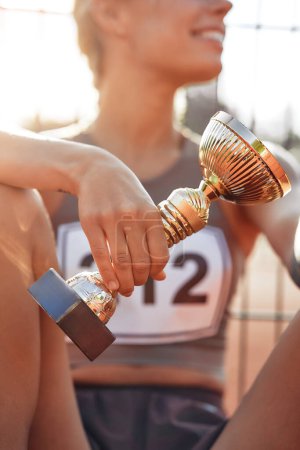 Photo for Woman winner champion in sportswear with a number at the stadium with a cup resting after the competition. Sports and Olympic Games, victory concept. - Royalty Free Image