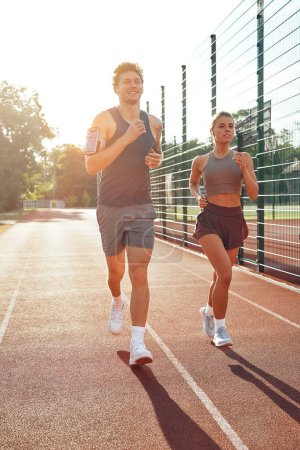 Photo for Couple in sportswear running at the stadium. Morning exercises and jogging. Sports and Olympic Games, active lifestyle. - Royalty Free Image