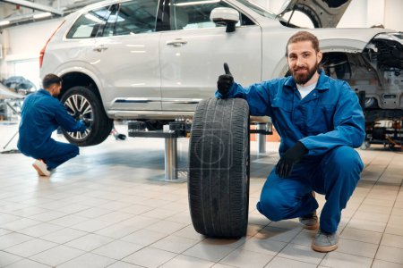 Photo for Car mechanic working in garage and changing wheel alloy tire. Repair or maintenance auto service. Mechanic holding a tire tire at the repair garage, replacement of winter and summer tires. - Royalty Free Image