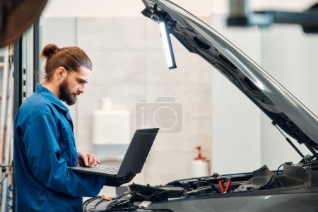 Photo for Mechanic in uniform repairing a car in a workshop. Auto mechanic detailed inspection of the car. Auto car repair service center. Car service, repair, maintenance concept. - Royalty Free Image