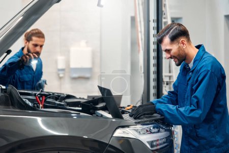Photo for Two mechanics are repairing a car in a workshop. Auto mechanic detailed inspection of the car. Auto car repair service center. Car service, repair, maintenance concept. - Royalty Free Image