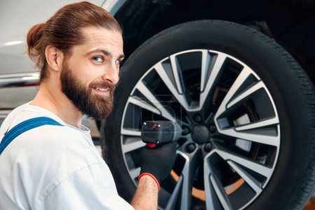 Photo for Car mechanic working in garage and changing wheel alloy tire. Repair or maintenance auto service. Mechanic holding a tire tire at the repair garage, replacement of winter and summer tires. - Royalty Free Image