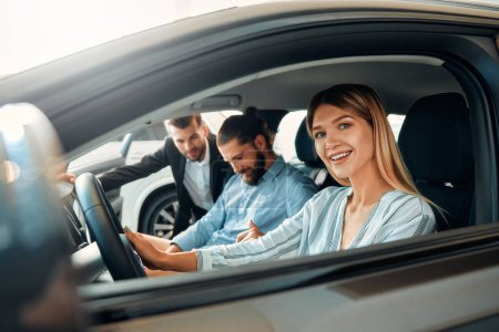 Photo for A couple is sitting in a car at a car dealership and receiving advice from a salesperson. Purchase, rental and insurance of a car. - Royalty Free Image