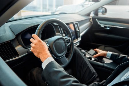 Foto de Foto recortada de un hombre de negocios con un traje negro conduciendo un coche con la mano en el volante. - Imagen libre de derechos