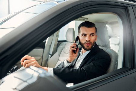 Photo for Male businessman in a black suit driving a car and talking on the phone. - Royalty Free Image