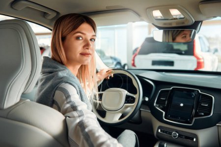 Foto de Una joven sentada en un coche en el asiento del conductor y mirando hacia atrás. Comprar, alquilar y asegurar un coche. - Imagen libre de derechos
