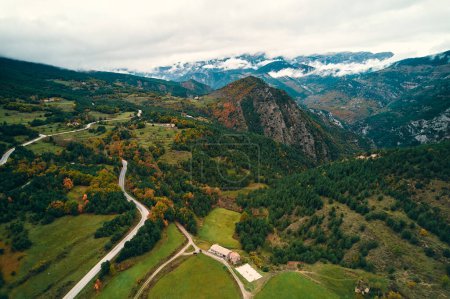 Téléchargez les photos : Vue aérienne d'une vallée de montagne avec une route serpentant à travers le paysage naturel. Nuages parsèment le ciel au-dessus, les plantes couvrent les pentes du terrain - en image libre de droit